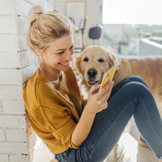 Woman smiling and looking at a smartphone with a dog in the background