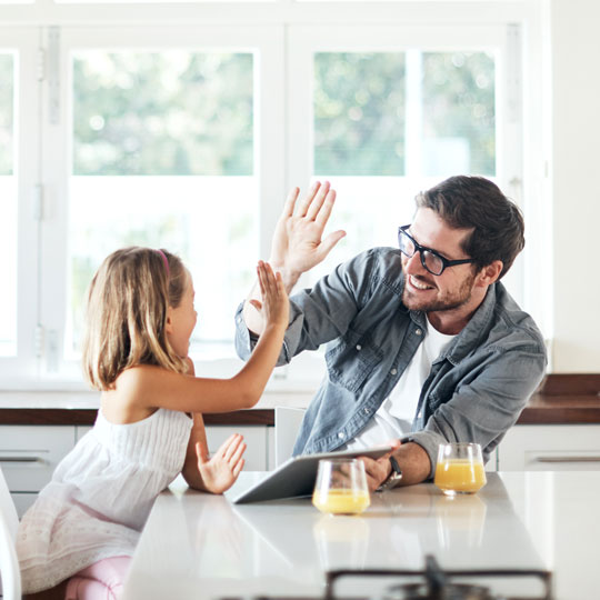 Father and daughter smiling and high-fiving in their kitchen