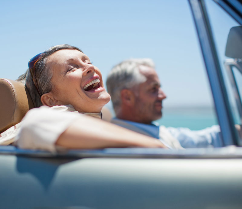 Older man and woman smiling and riding in a convertible