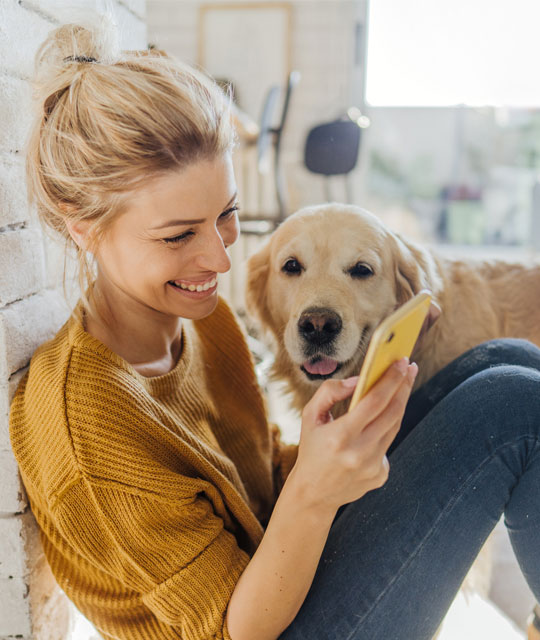 Woman looking at a smartphone and smiling with dog in the background