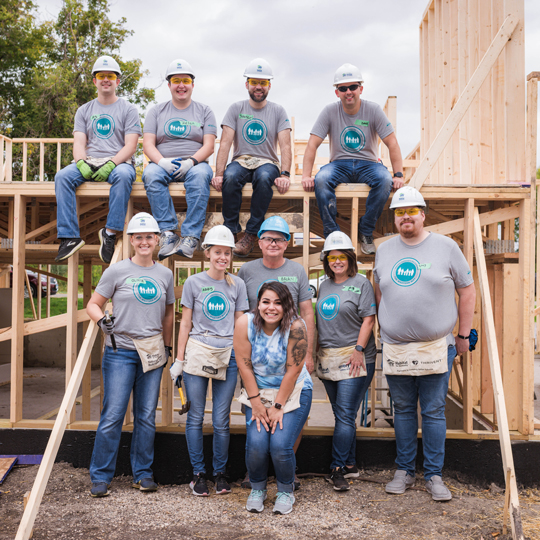 Group of volunteers smiling and standing in front of a house frame