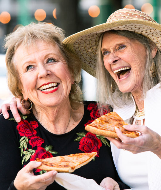 Two women smiling with pizza